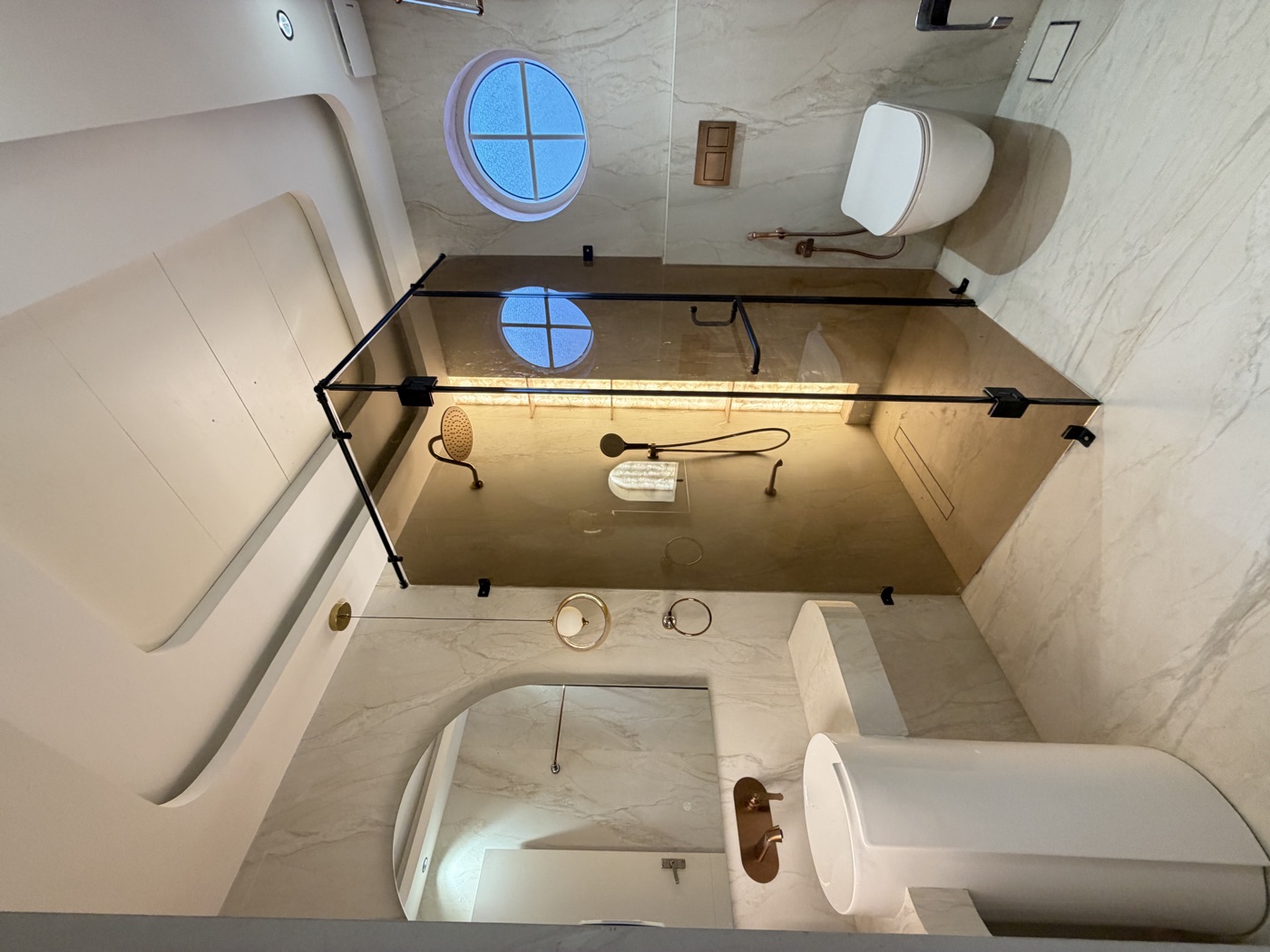 Completed bathroom with a glass shower enclosure, arched mirror, pedestal basin and circular window