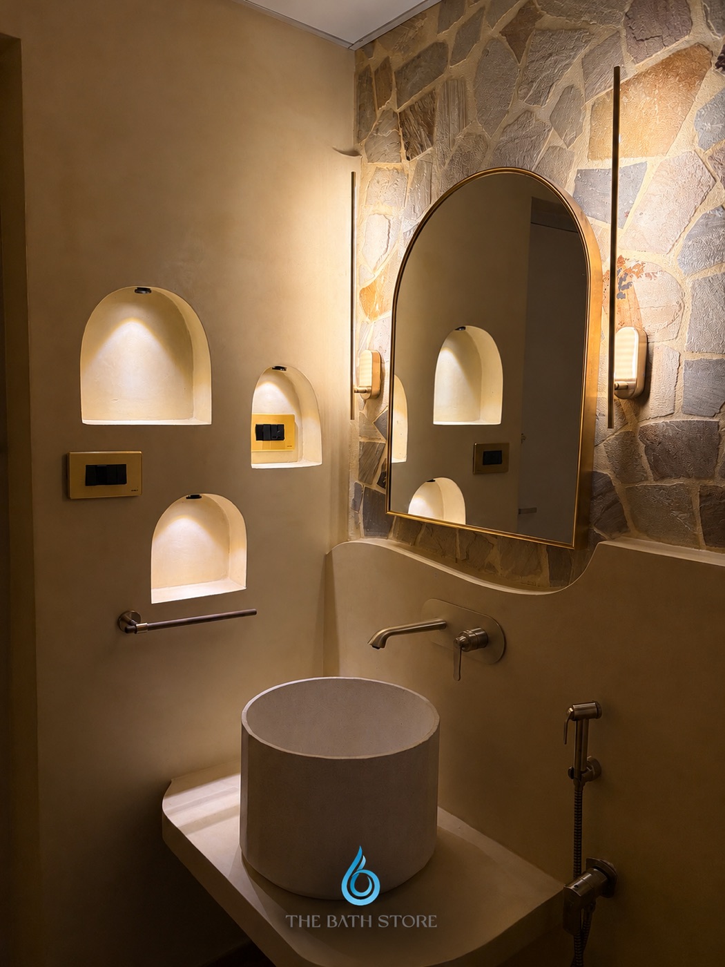 A completed vanity with an arched mirror, textured wall and illuminated niches